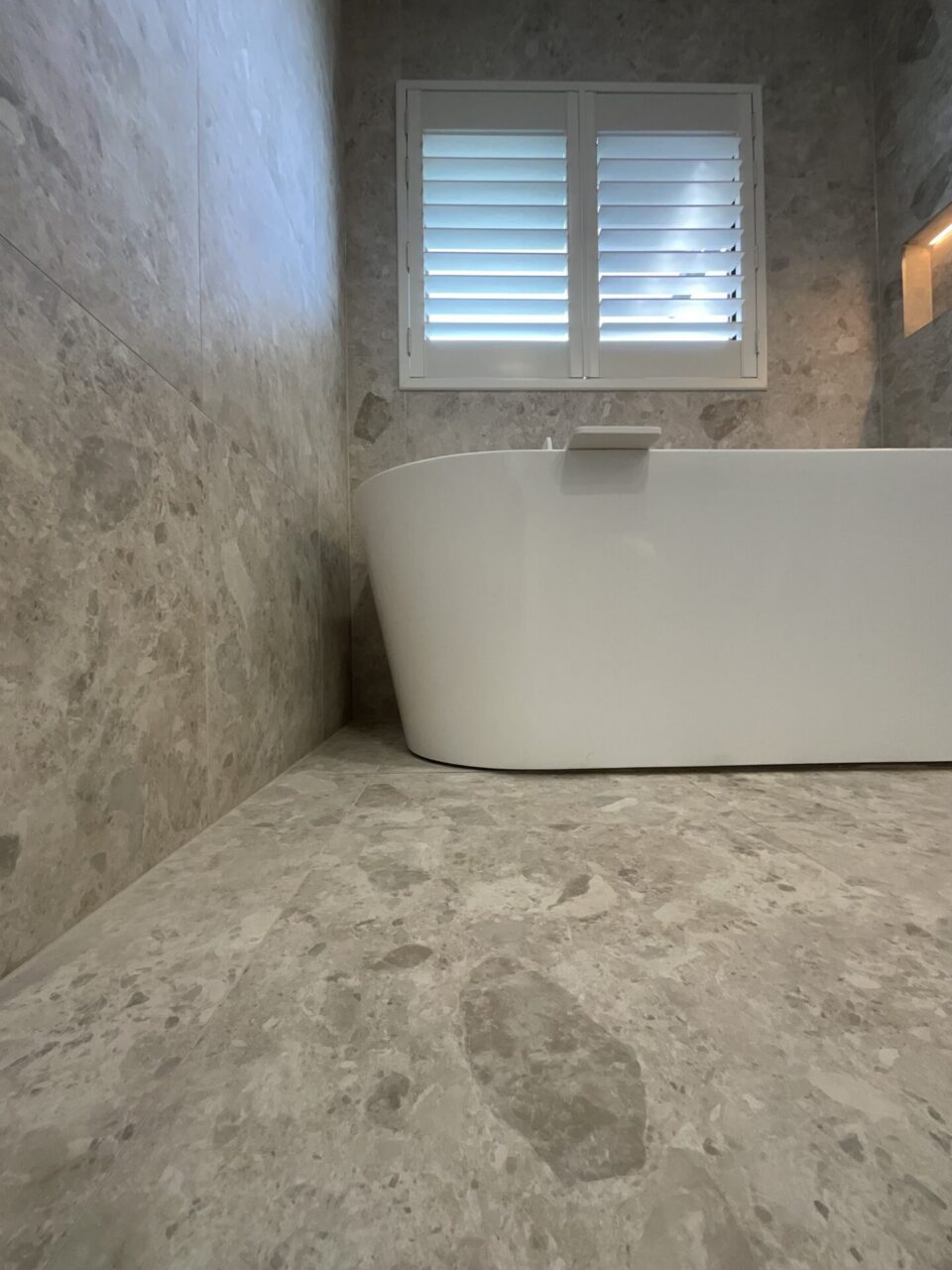 Palm back to wall freestanding bath beneath plantation shutters in a luxury bathroom